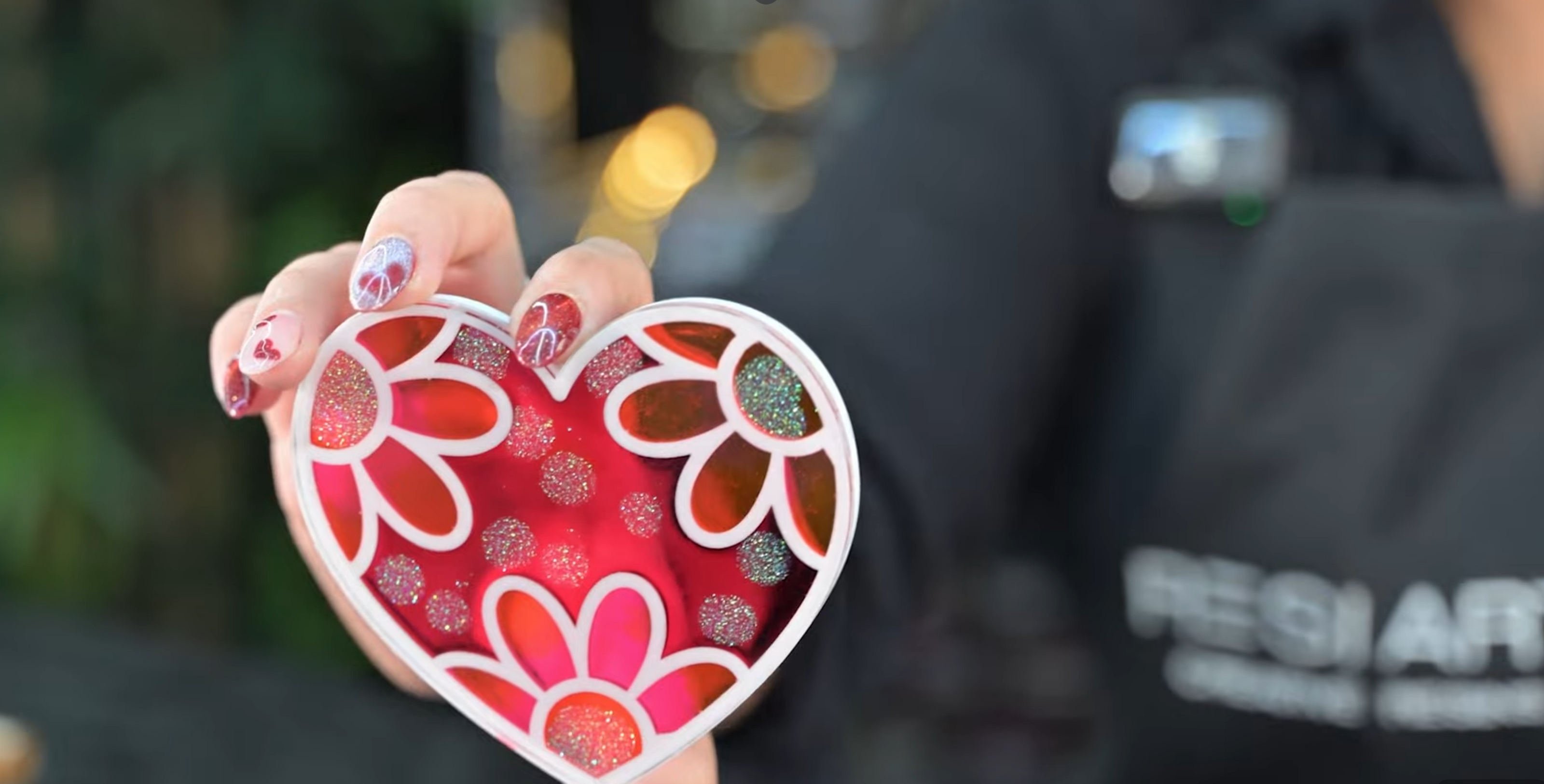 Heart-shaped resin template with floral design held by a person wearing a black jacket with 'Resi Art' text.